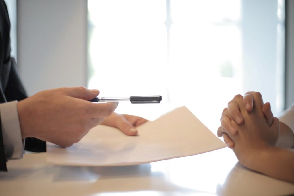 A person offering a pen and mortgage documents to another individual.