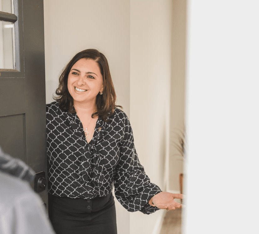 A Female Homeowner in a Black and White Ensemble Opening the Door for a Potential Buyer