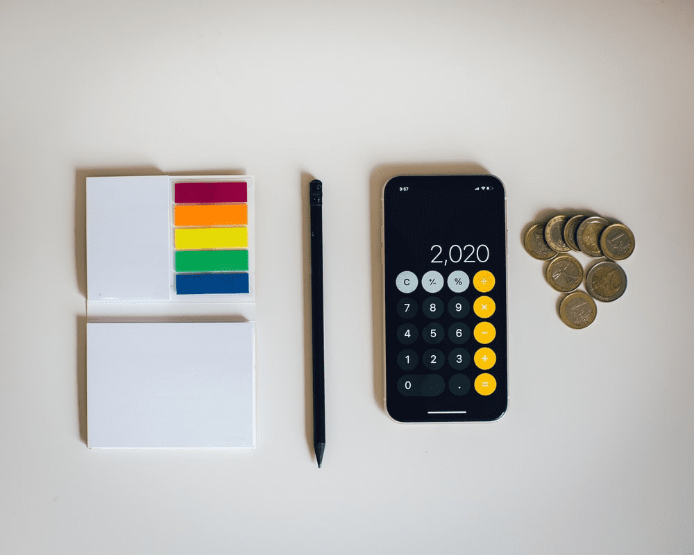 a smartphone, note pad, and coins on a desk