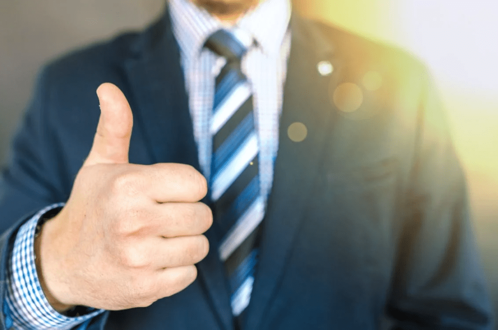 A photo showing a person in a blue suit performing a thumbs-up gesture.