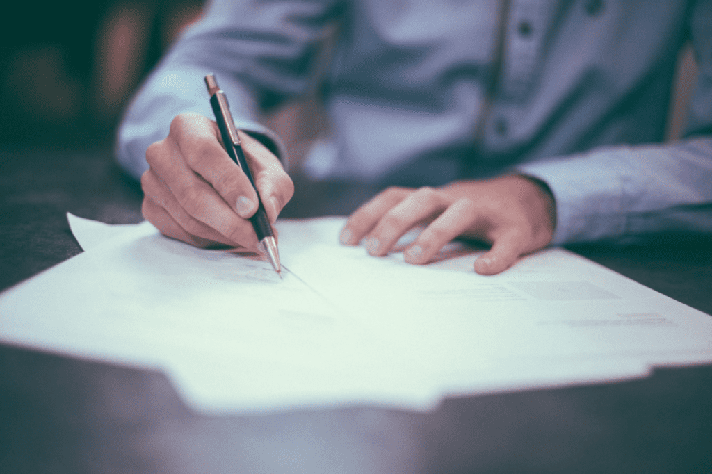 A photo showing a person holding a pen over a document