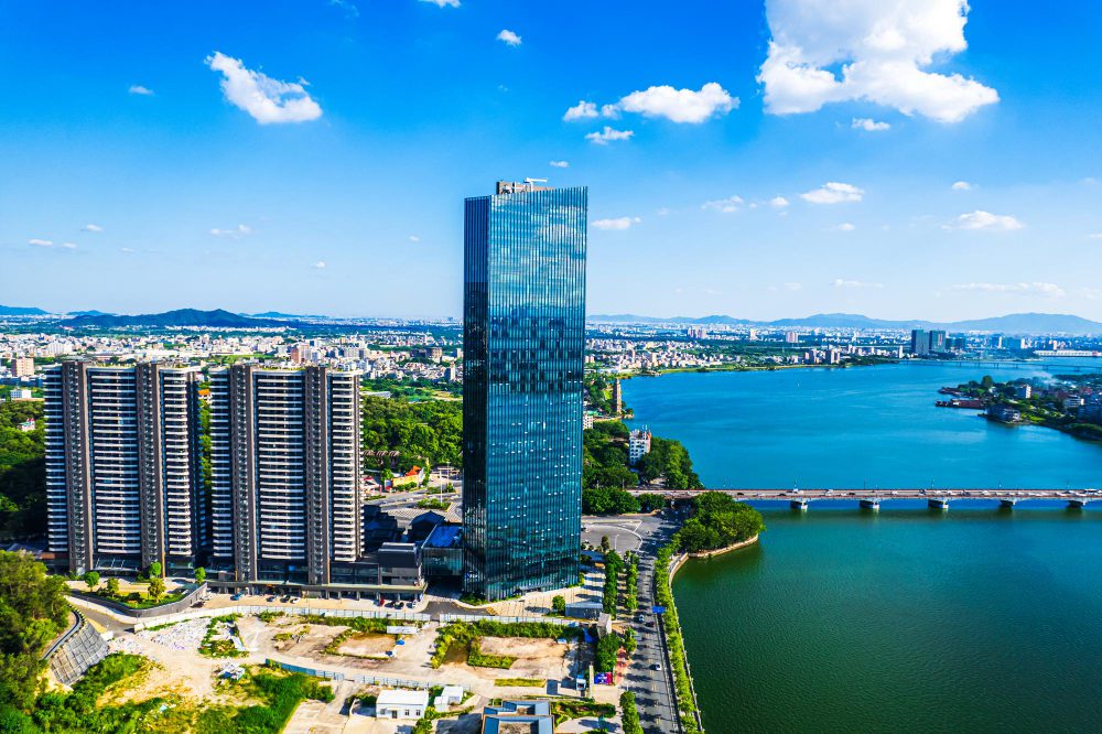 Modern skyscraper towering beside apartment buildings near a river in an urban landscape.