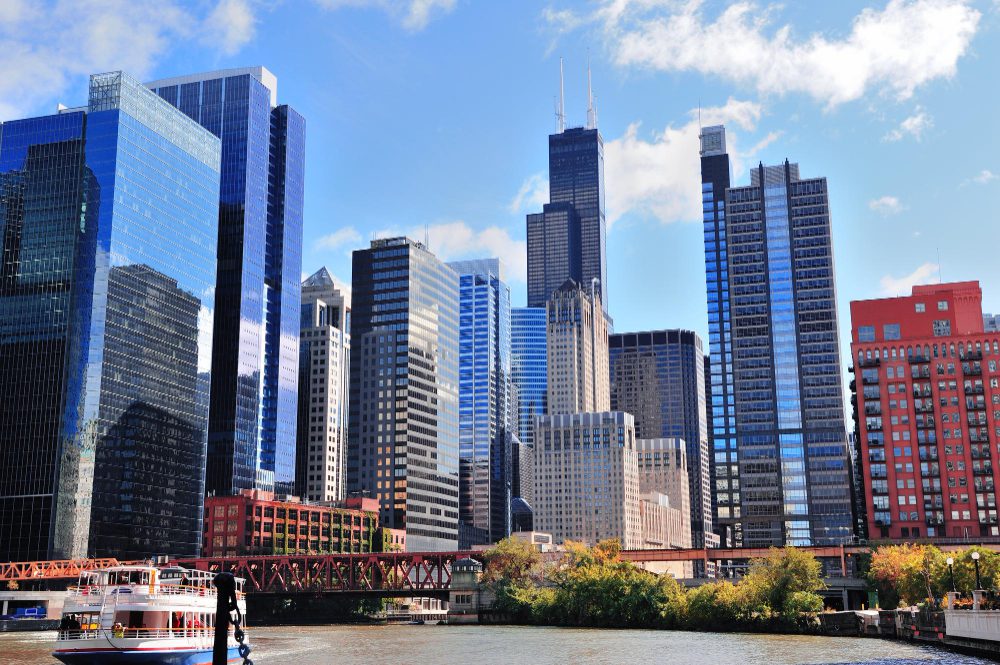 Chicago skyline with a tour boat on the river, featuring modern skyscrapers against a backdrop of blue skies with scattered clouds.