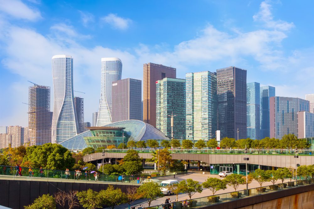 Modern city skyline with skyscrapers and a glass building, under a clear blue sky.