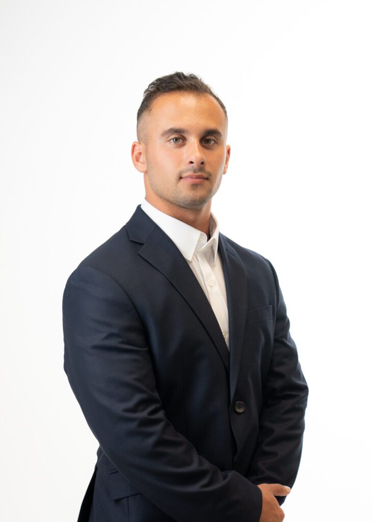 A man in a dark suit and white shirt, posing against a white background.