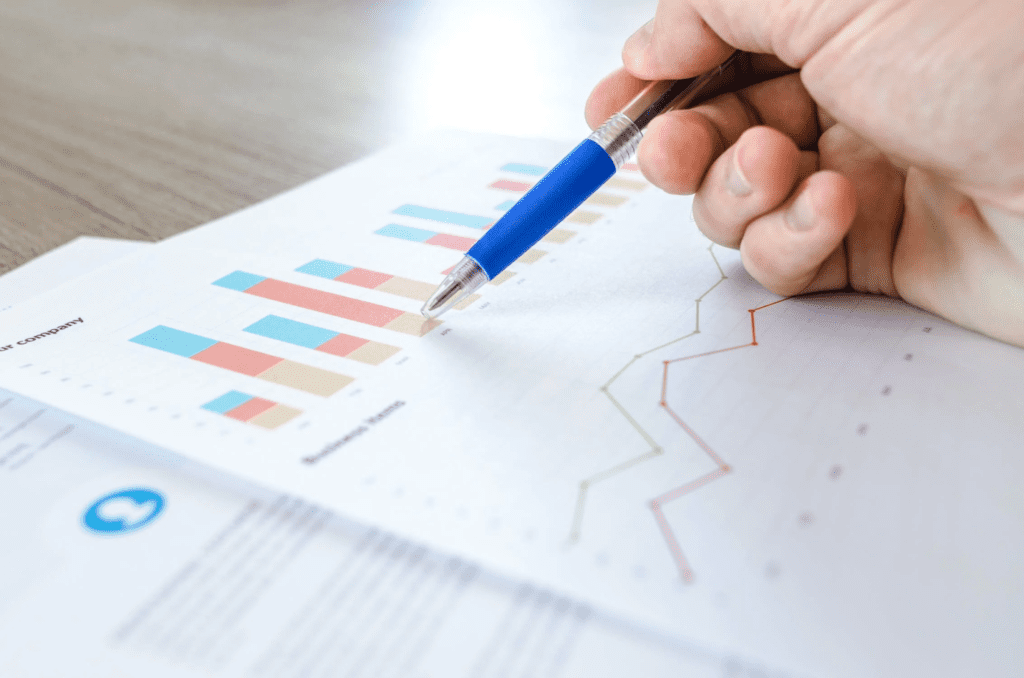 A photo showing a person holding a pen over a document. Caption: A person using a pen to point to graphs on a document.