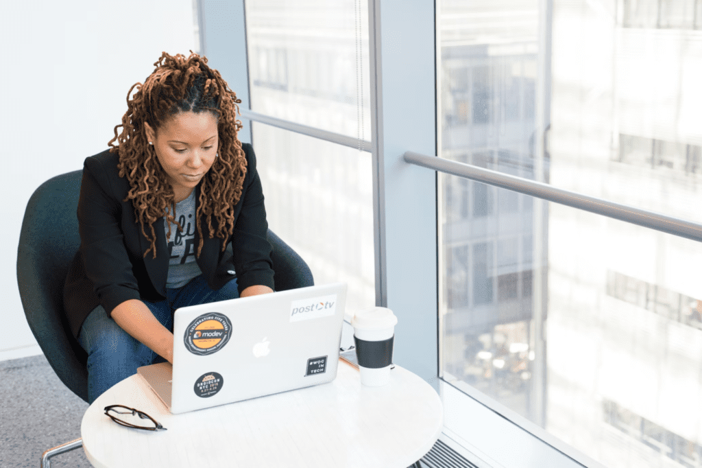 A photo showing a woman using a computer by a window.