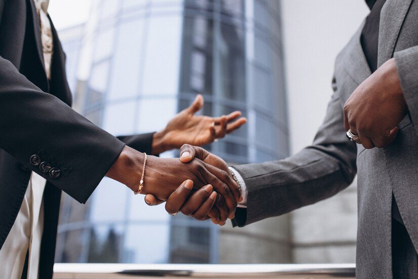 Two professionals shaking hands in front of a building with reflective windows.