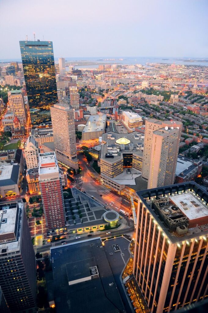 Aerial view of a cityscape at dusk with illuminated streets and a mix of modern and traditional buildings.