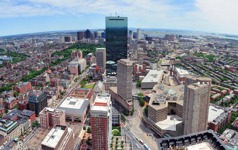 Aerial view of a dense urban skyline with towering buildings in various architectural styles, under a clear sky.