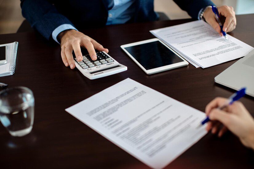 Two individuals reviewing documents and performing calculations at a business meeting.