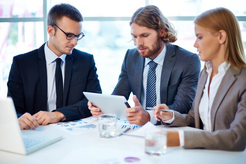 Three professionals in a meeting discussing over a digital tablet.