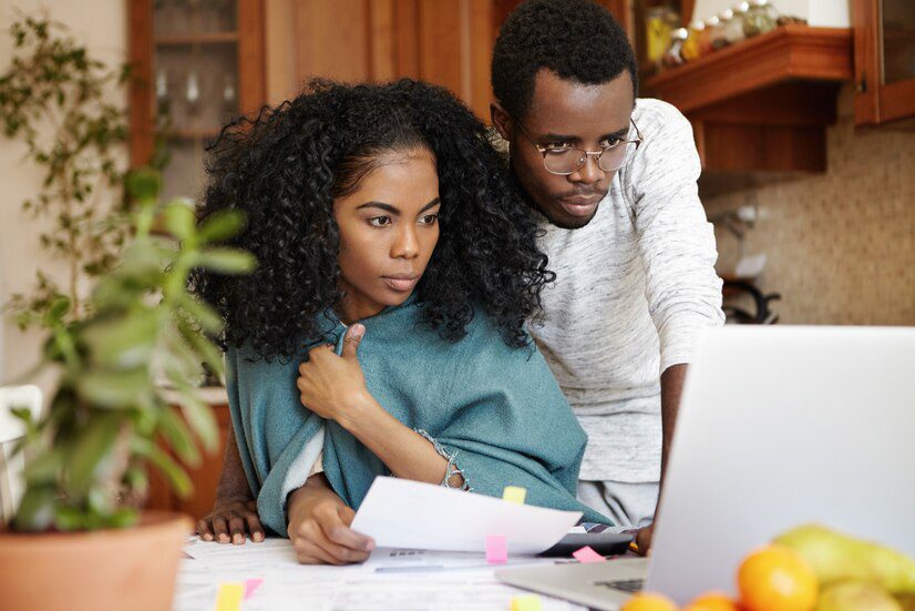 Two individuals engaged in focused work at a laptop in a home environment.