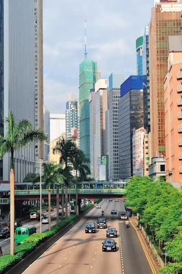 Urban street with vehicles flanked by high-rise buildings under a clear sky.