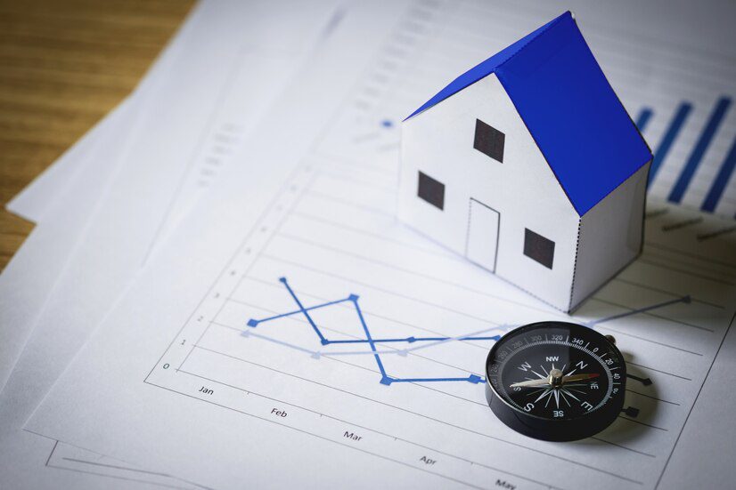 A paper house model on top of a graph with data trends, alongside a compass, representing real estate market analysis and direction.