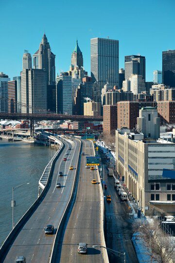 A daytime view of a cityscape with a highway leading towards skyscrapers under a clear blue sky.