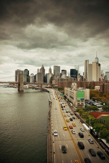 An overcast day in a city with a view of a river, a bridge, and skyscrapers under a cloudy sky.