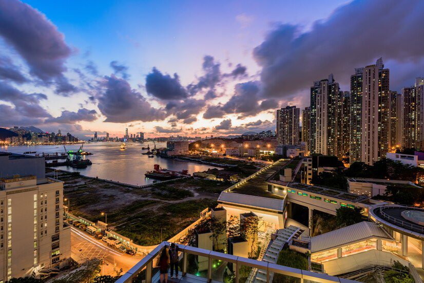 Evening skyline of a modern city with residential towers and a waterfront, under a dramatic cloudscape.