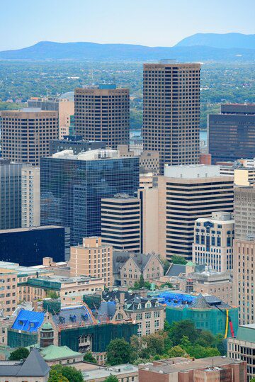 Aerial view of a downtown area with a mixture of modern high-rises and older buildings against a backdrop of distant hills.