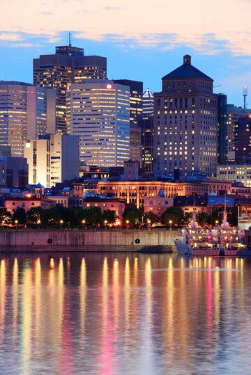 City skyline at dusk with building lights reflecting on water.