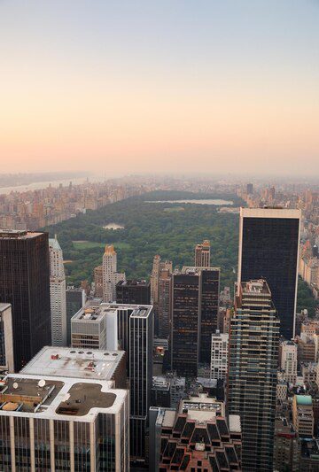 Aerial view of a city skyline with central park surrounded by tall buildings at dusk.