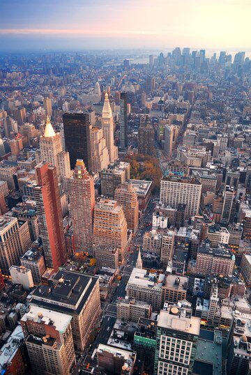 Aerial view of a dense urban skyline at dusk with skyscrapers and city streets.