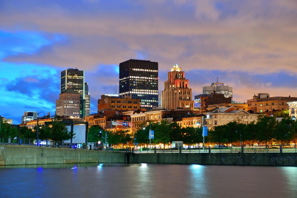 Evening skyline of a city with illuminated buildings reflected in a calm river.