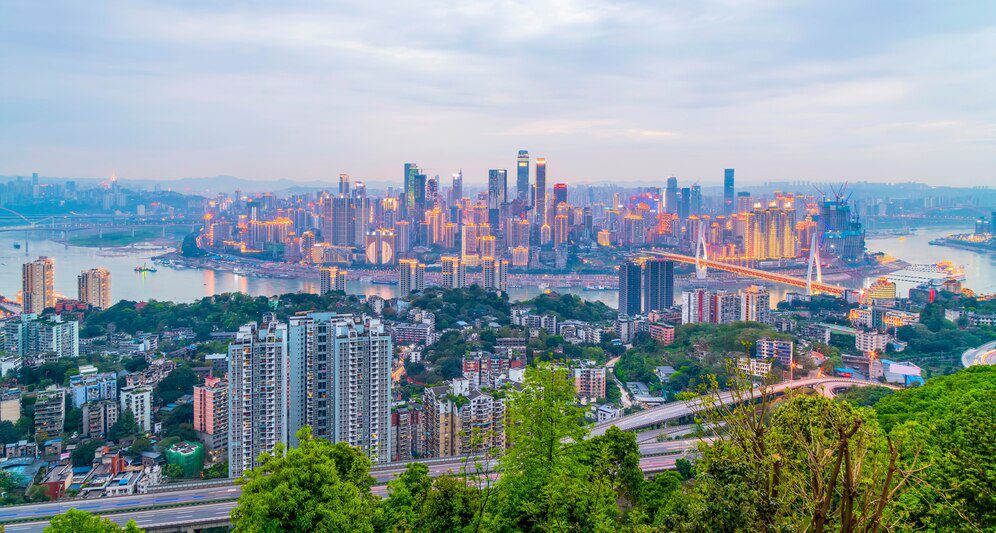 Panoramic view of a modern city skyline at dusk with skyscrapers and a river.