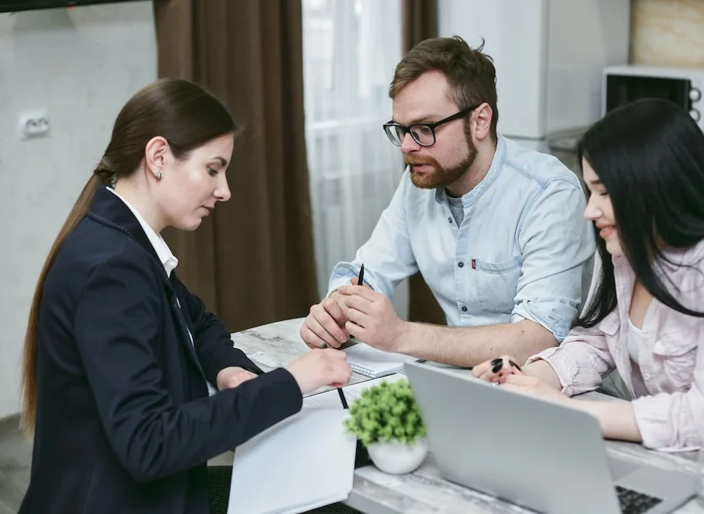 Three professionals engaged in a discussion at a meeting with a laptop and documents on the table.