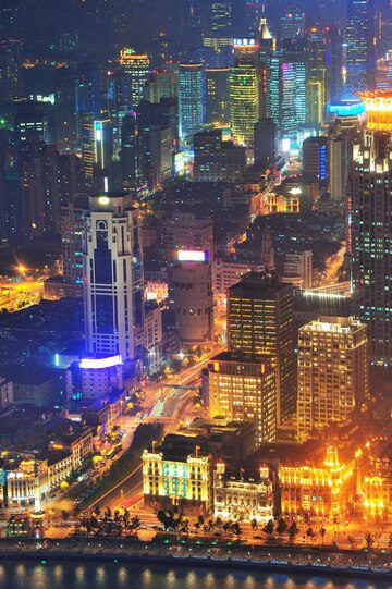 Aerial night view of a vibrant cityscape illuminated with numerous lights from skyscrapers and busy streets.