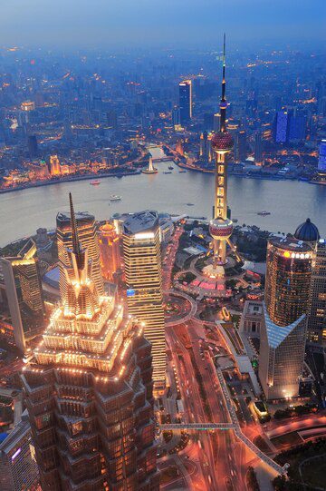 Aerial view of a vibrant city skyline at dusk with illuminated skyscrapers and a winding river.