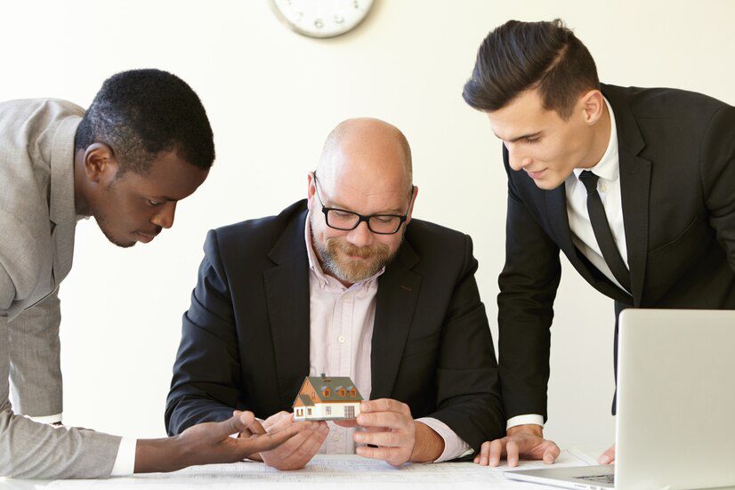 Three professionals examining a small model house and documents on a table.