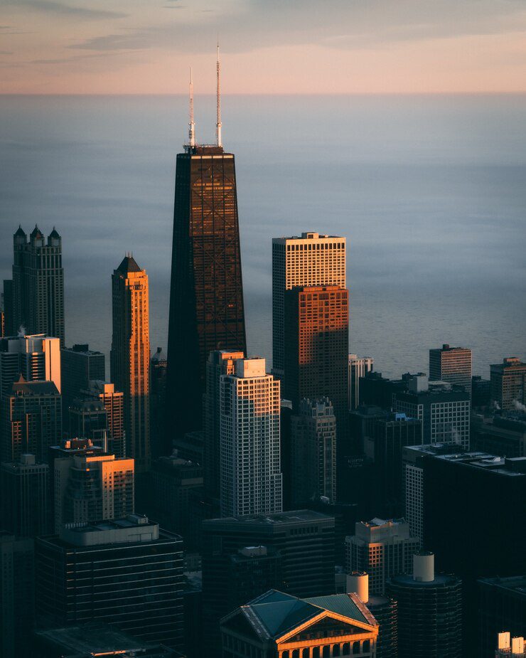 Golden light casting over a city skyline with a prominent skyscraper standing out against a backdrop of clouds.