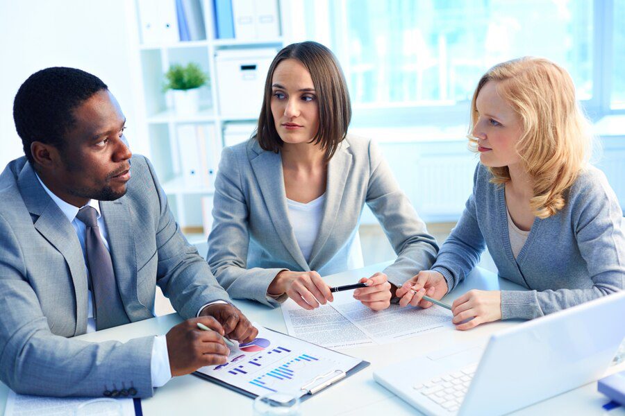 Three professionals discussing documents at a meeting in the office.