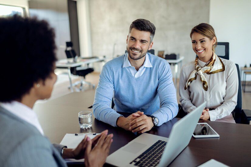 Three professionals in a meeting, with two smiling at the person across the table.