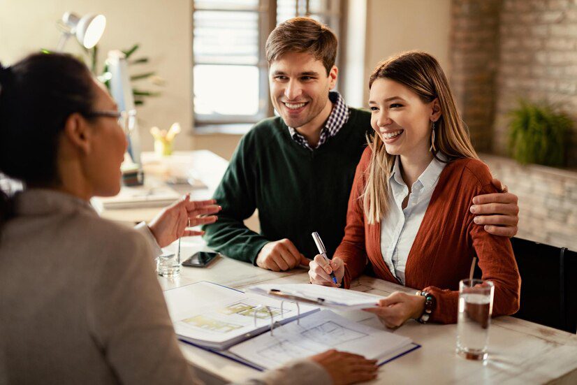 Two people smiling during a meeting with another person, with documents on the table suggesting a professional engagement.