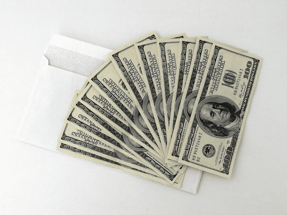 Twelve 100 U.S. Dollar banknotes on an envelope on a white table