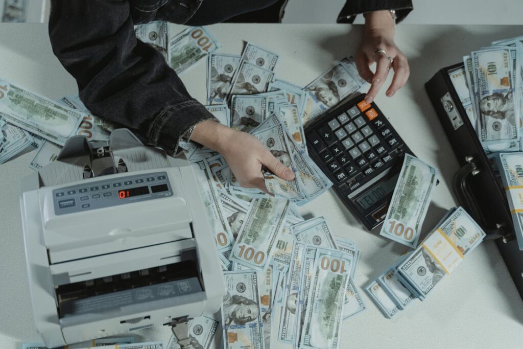 A person holding dollar bills while using a calculator and a money counter