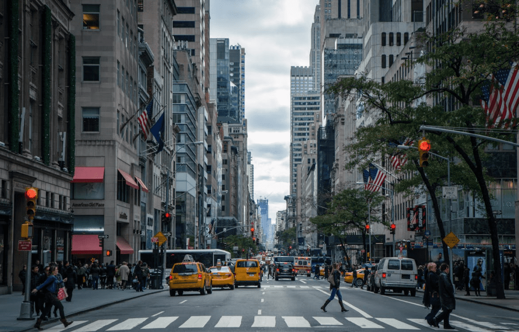 A photo of a street with tall buildings, vehicles, and people moving around