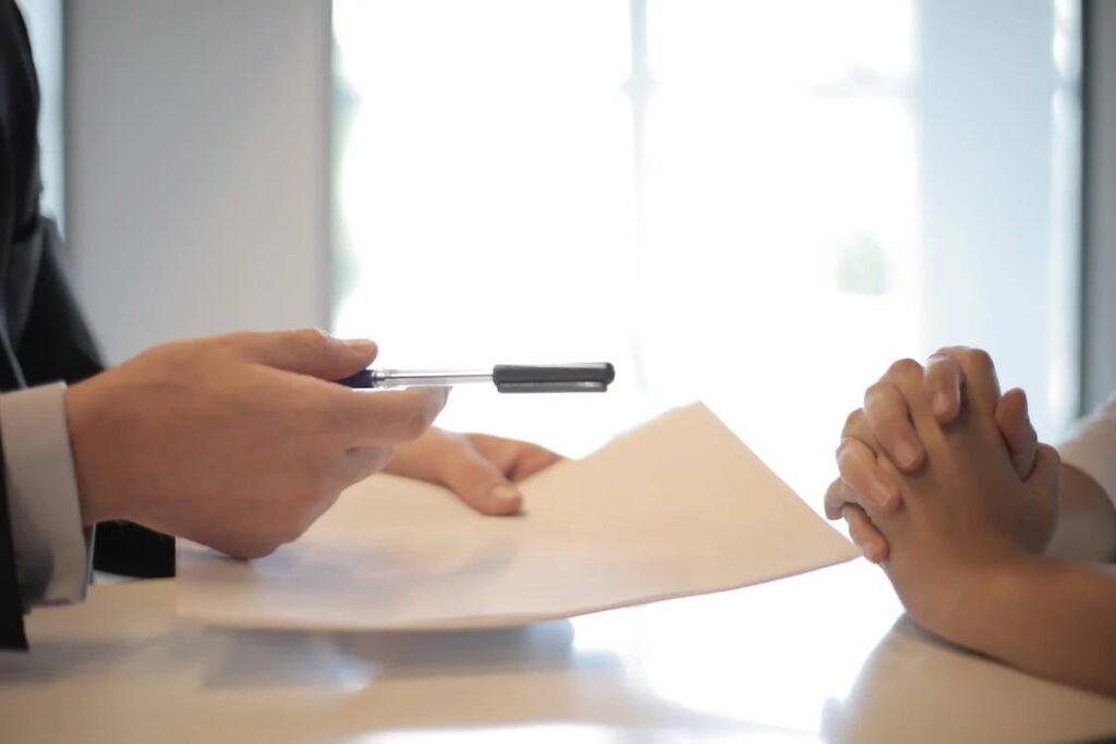 A person handing a contract and pen to another person