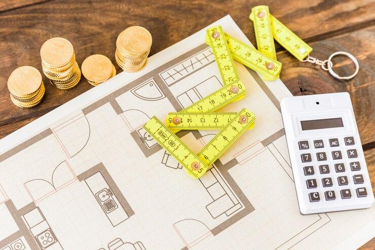 High-angle view of a measuring tape, calculator, stacked coins, and blueprint