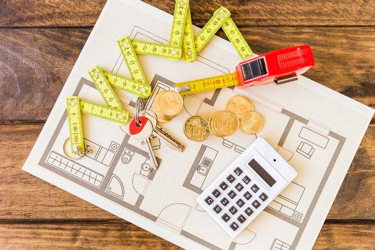 Elevated view of a measuring tape, coins, keys, a calculator, and a blueprint representing financial planning