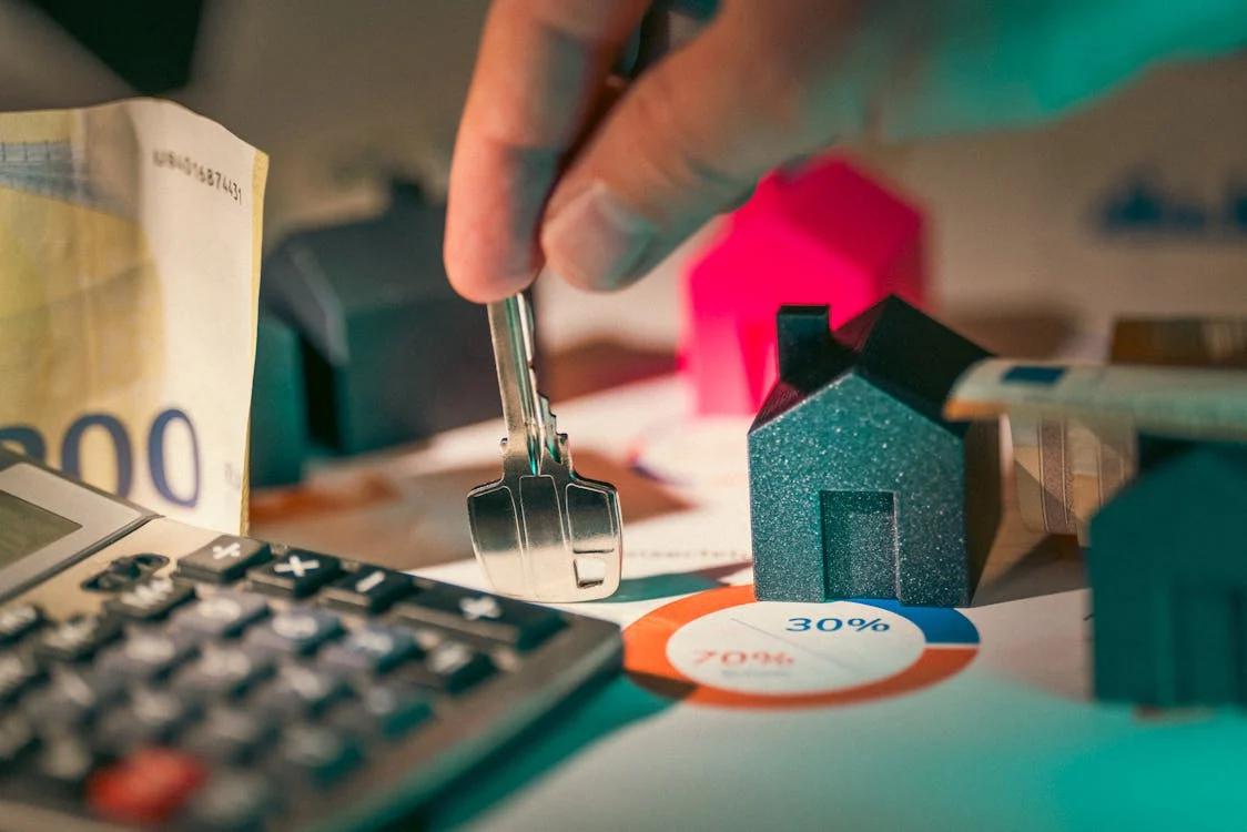 Hand holding keys next to a calculator and miniature houses