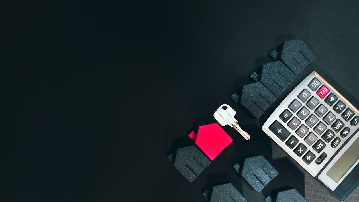 A calculator and key next to some miniature houses 