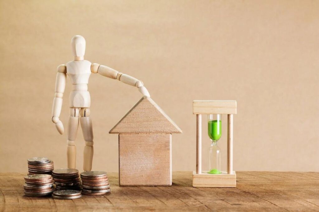 A miniature person standing with a house and hourglass with some coins in front of it.