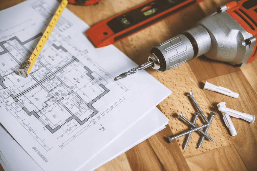 A renovation plan with some tools such as screw, measurement scale, drill machine, etc. on a wooden surface