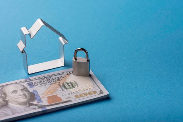 A small metal house outline with a lock placed on 100 US dollar banknotes bundle