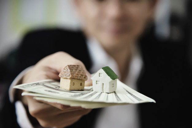 A person holding a bundle of US dollars with two miniature homes on it