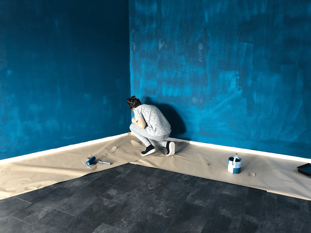 A person covering the floor while painting a wall blue