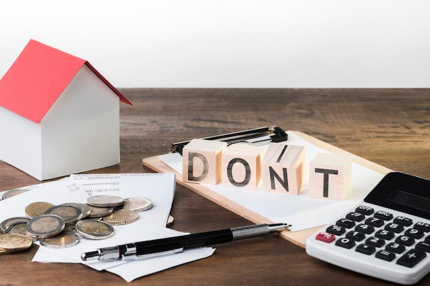 A red and white mini house, with coins, a pen, a calculator, and DON’T written using wooden blocks placed on a table